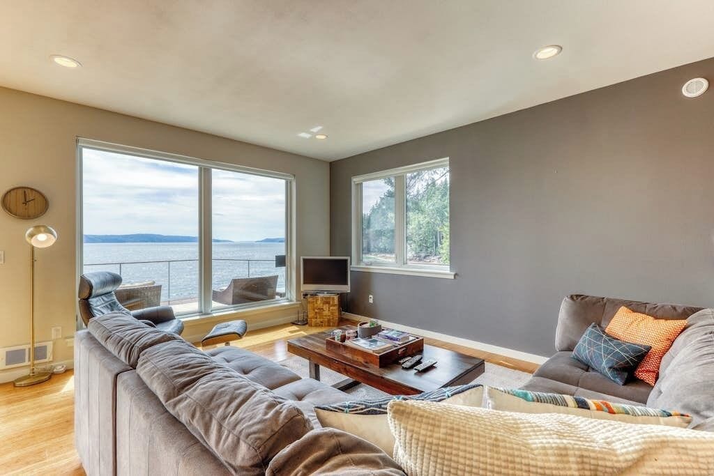 A living room with a large window overlooking a body of water, a sofa, a coffee table, and a television.