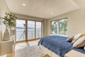 A bedroom with a large bed, a view of the sea, and a tripod in the corner. - 4BR Bayview Dog Friendly - Balcony - Firepit (Brinnon)