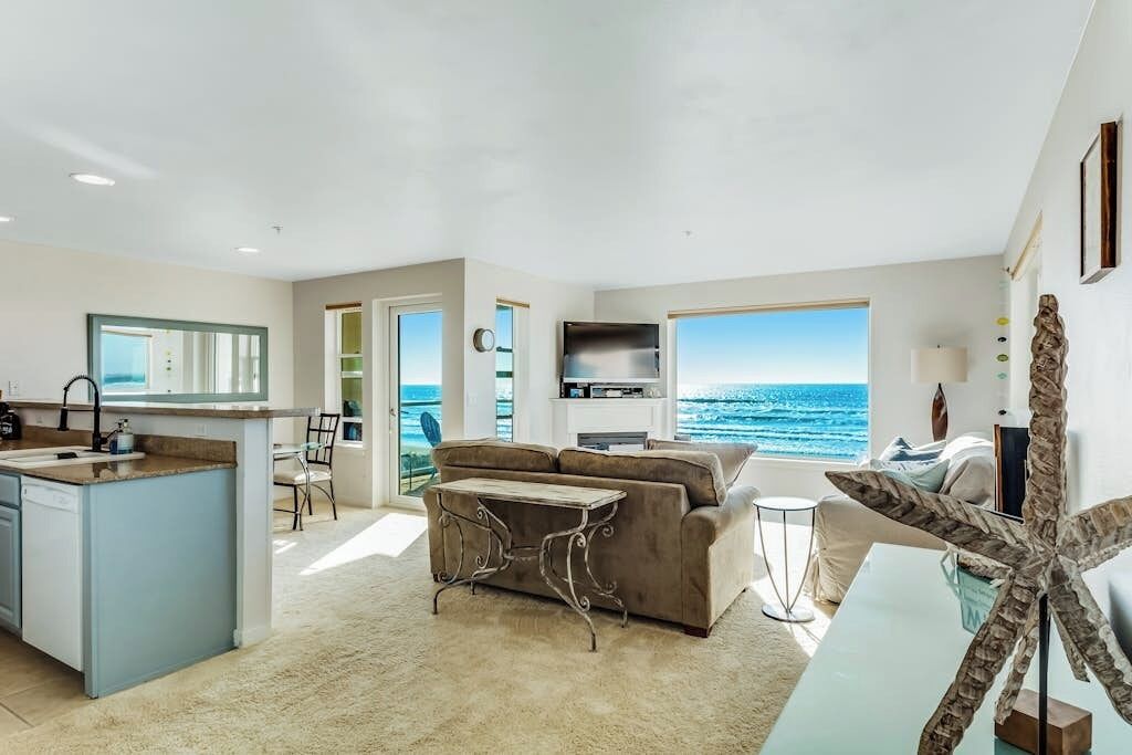 A modern living space with a kitchen, seating area, and a large window overlooking the ocean.