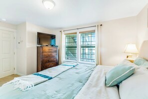 Un dormitorio con cama, cómoda, televisor y ventana con cortinas.