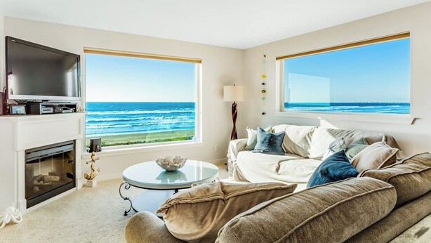 Een woonkamer met een groot raam met uitzicht op de oceaan, een open haard en een moderne bank.