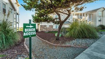 A sign indicating beach access, surrounded by a landscaped area with a tree and shrubs.
