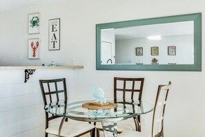 Un comedor con una mesa redonda de vidrio, cuatro sillas, un espejo y una obra de arte en la pared.