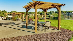 Een terras buiten met houten pergola's, zithoekjes en een verzorgd gazon.