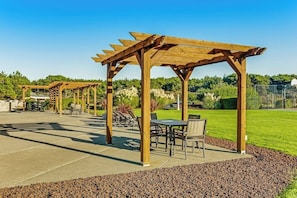 Un espace extérieur aménagé en terrasse, doté de pergolas en bois, de coins salon et d’une pelouse bien entretenue.