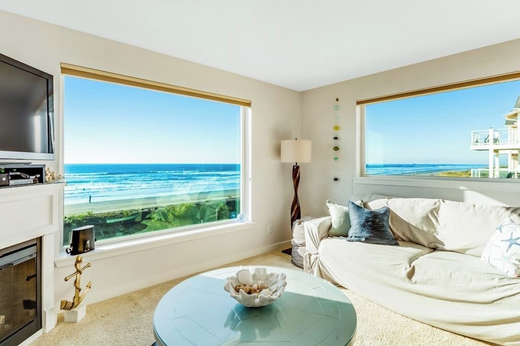 Ein Zimmer mit großem Fenster mit Blick auf das Meer, einer Couch, einem kleinen Tisch mit einer Schüssel und einem Fernseher.