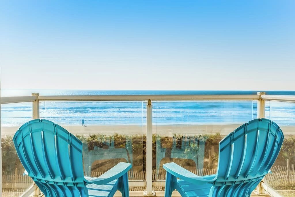 A balcony with two chairs facing a beach view.