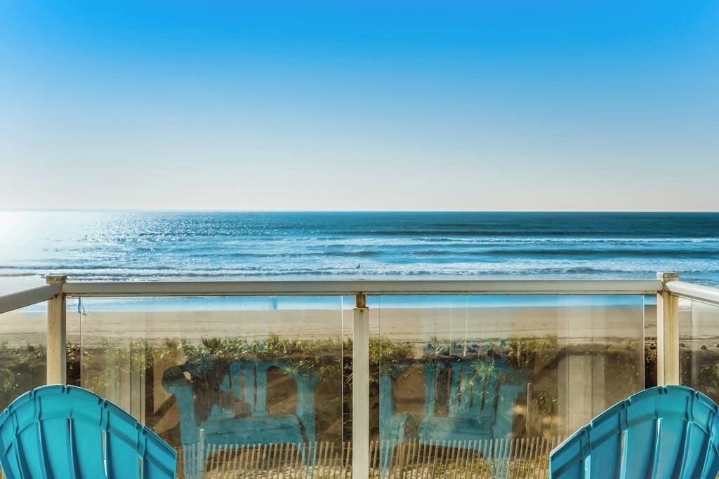 Ein Balkon mit Blick aufs Meer, zwei Stühle und einer Glasbrüstung.