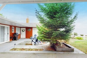 A covered porch with a potted evergreen tree, outdoor seating, and a grill. - Prime 1BR Oceanfront Dog Friendly - Patio - Washer Dryer (Port Angeles)