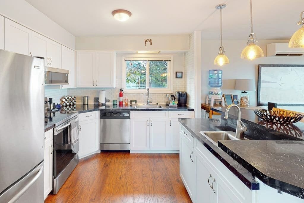 A modern kitchen with white cabinets, stainless steel appliances, and a black granite countertop.
