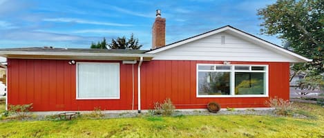 Une maison de plain-pied à l’extérieur rouge, avec une cheminée et un petit jardin devant.