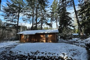 Una cabana amb el terra cobert de neu, envoltada d'alzines altes.