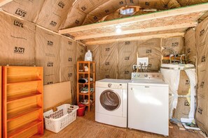 Een wasserette met een wasmachine, droger, houten planken en een wastafel.