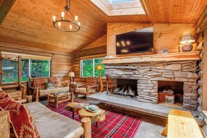 Interior d'una cabana de fusta amb una llar de pedra, mobles de fusta i un televisor pantalla plana muntat per sobre de la llar.
