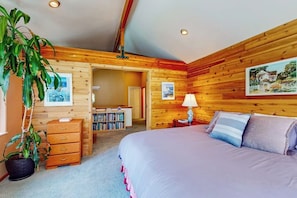 Ein Zimmer mit einem Bett, einem Nachttisch, einer Lampe, einem Bücherregal und einer Topfpflanze.