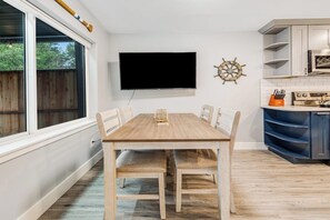 A dining area with a wooden table and chairs, a flat-screen TV mounted on the wall, and a kitchen with blue cabinets and a wooden countertop. - Modern 3BR Dog Friendly - Hot Tub - Patio (Westport)