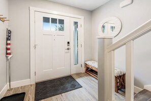 A hallway with a white door, a doormat, a small bench, and a round mirror on the wall. - Modern 3BR Dog Friendly - Hot Tub - Patio (Westport)