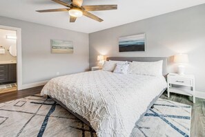 Une chambre à coucher avec un lit, des tables de chevet, un ventilateur de plafond et des œuvres d’art accrochées aux murs.
