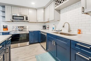 A modern kitchen with stainless steel appliances, white and blue cabinetry, and a white-tiled backsplash. - Modern 3BR Dog Friendly - Hot Tub - Patio (Westport)