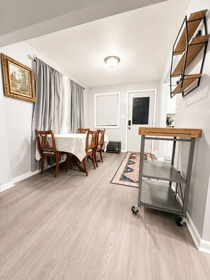 A dining area with a table and chairs, a rug, and a wall-mounted shelf unit. - Modern Cozy Stay Near
Downtown, Blossom & Cuyahoga Valley National Park (Cuyahoga Falls)