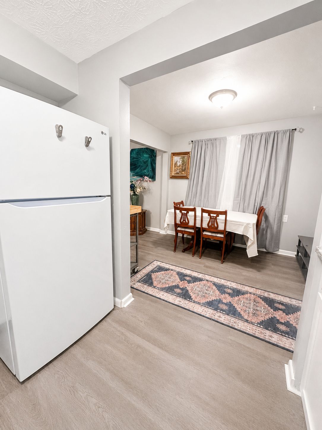 Una cocina compacta con un refrigerador blanco, un comedor con mesa y sillas, y una alfombra estampada en el suelo.