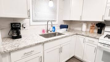 A modern kitchen with white cabinets, a granite countertop, a built-in oven, and a window with blinds.