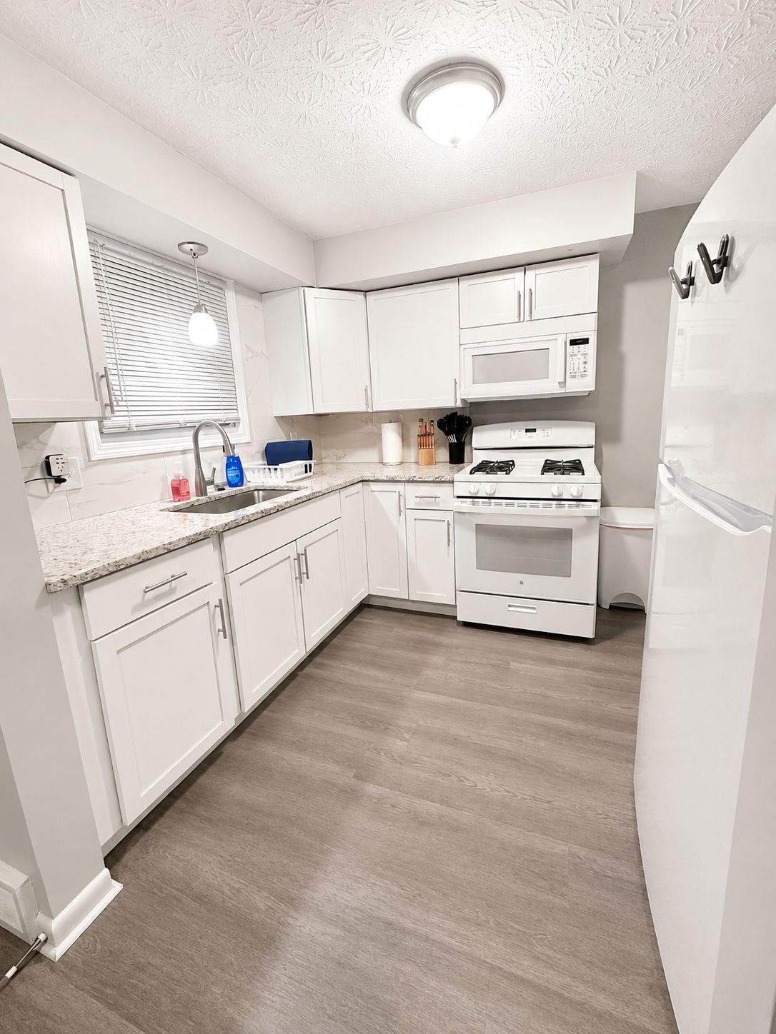 Una cocina moderna con armarios blancos, microondas integrado, estufa a gas y refrigerador.