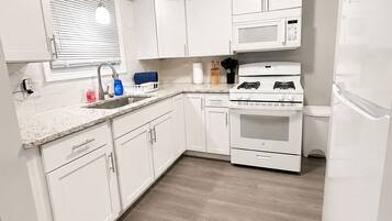 Una cocina moderna con armarios blancos, microondas integrado, estufa a gas y refrigerador.