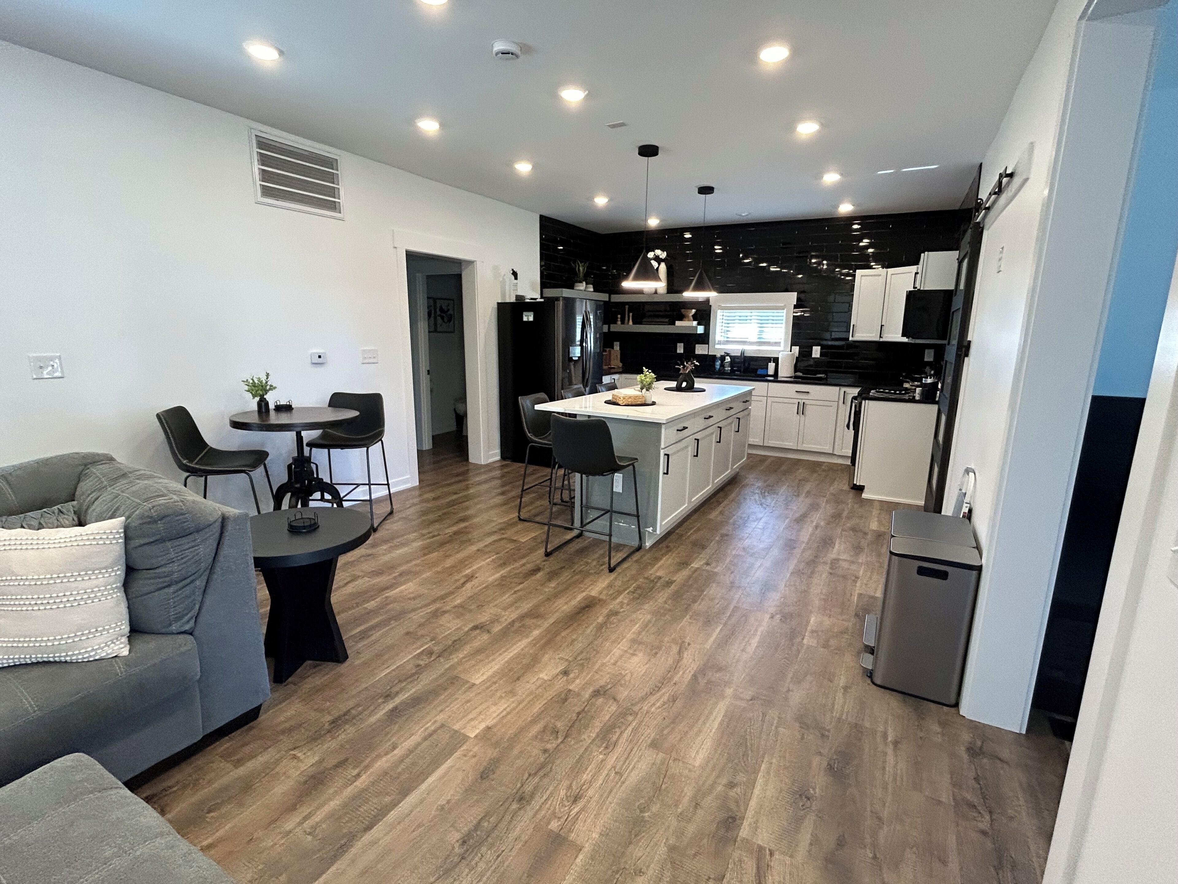 A modern kitchen with a central island, dining area with a sofa and chairs, and a hallway leading to another room.