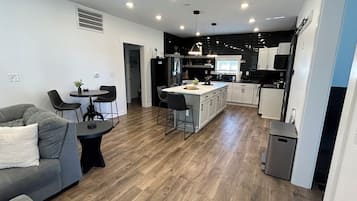 A modern kitchen with a central island, dining area with a sofa and chairs, and a hallway leading to another room.