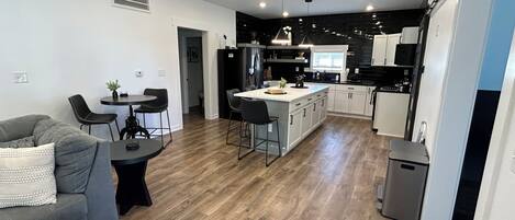 A modern kitchen with a central island, dining area with a sofa and chairs, and a hallway leading to another room.