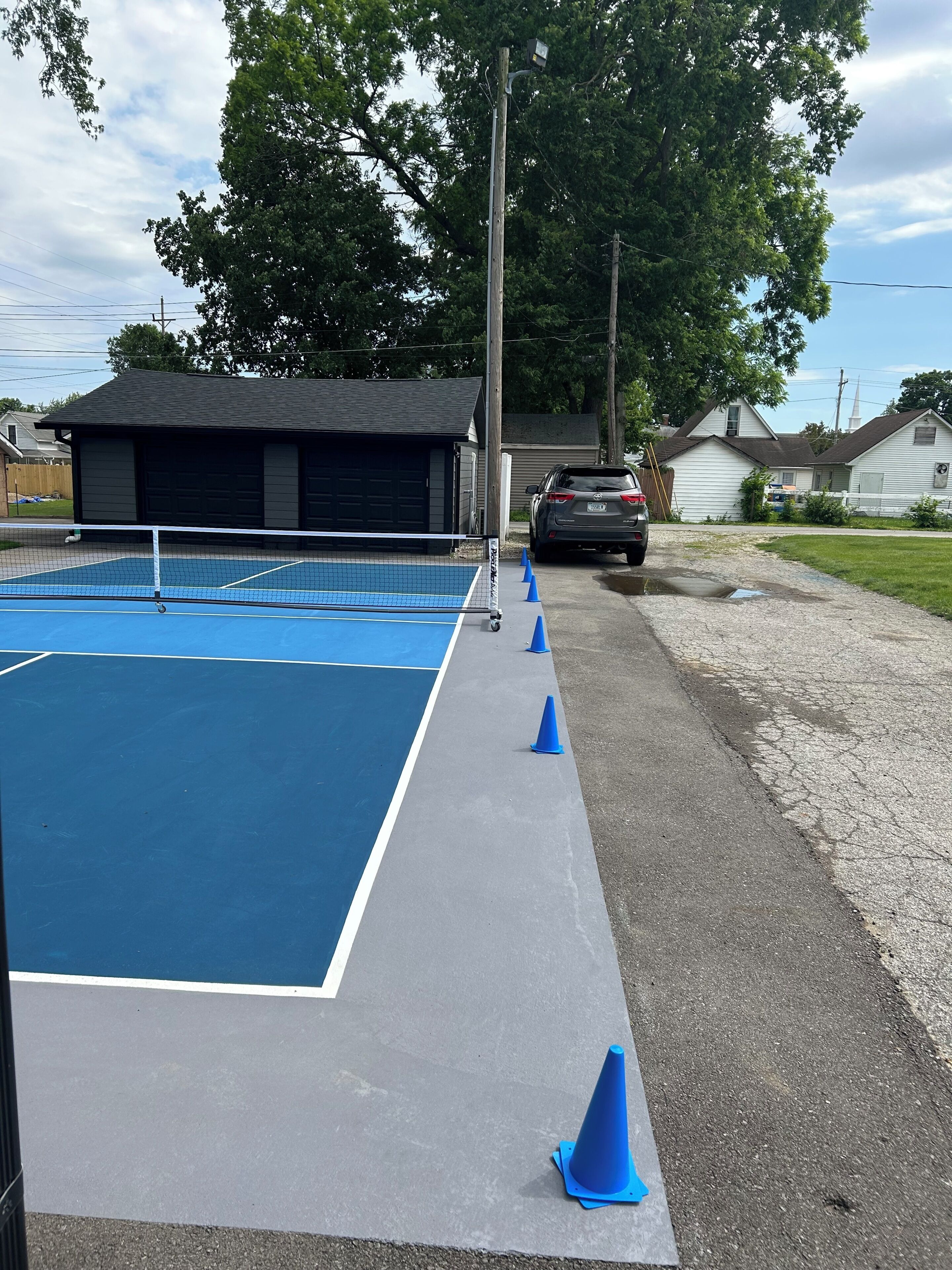 A tennis court with a net, surrounded by a gravel path and blue traffic cones.