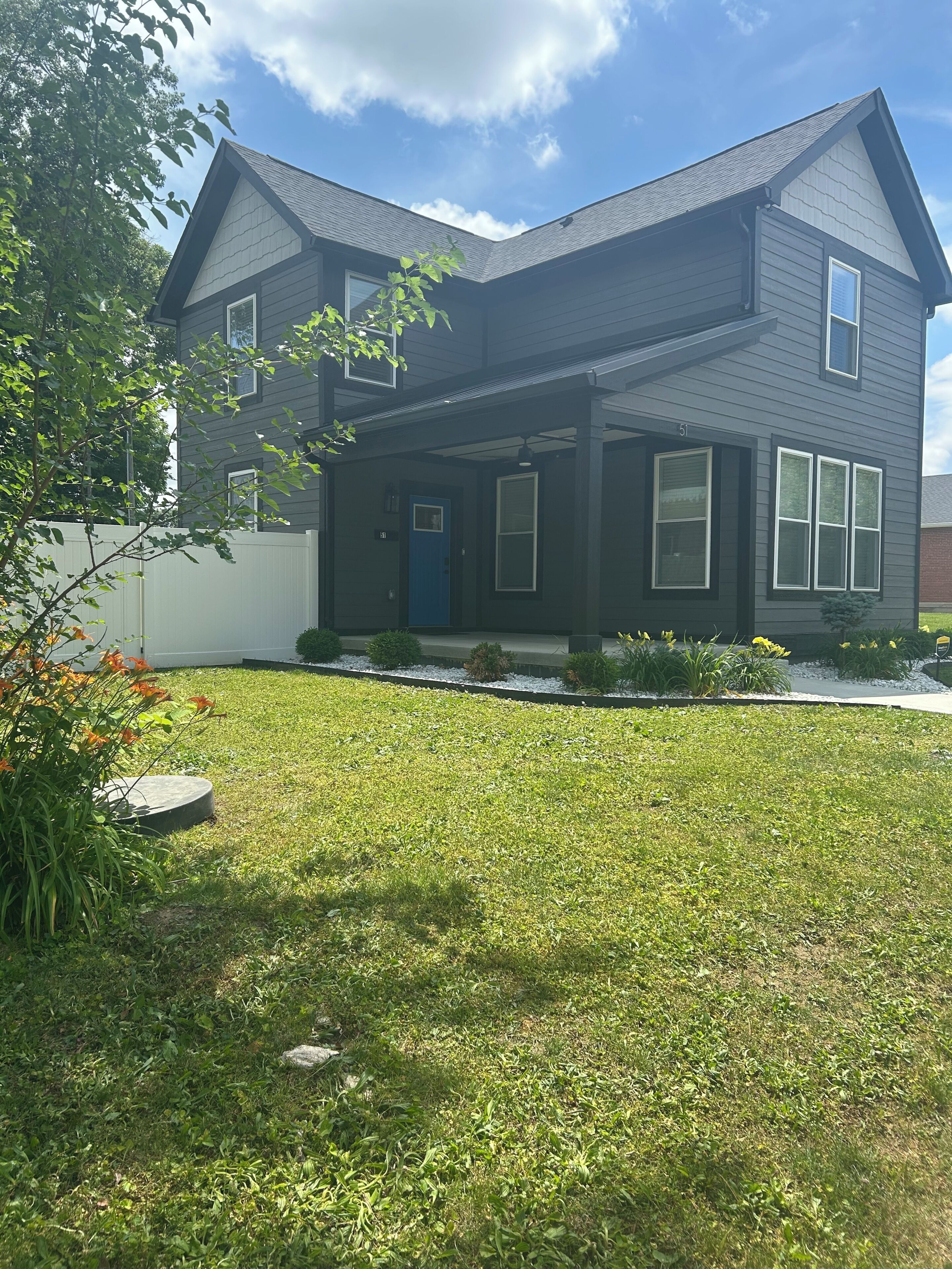 A two-story house with a dark exterior, a blue front door, and a well-maintained lawn.