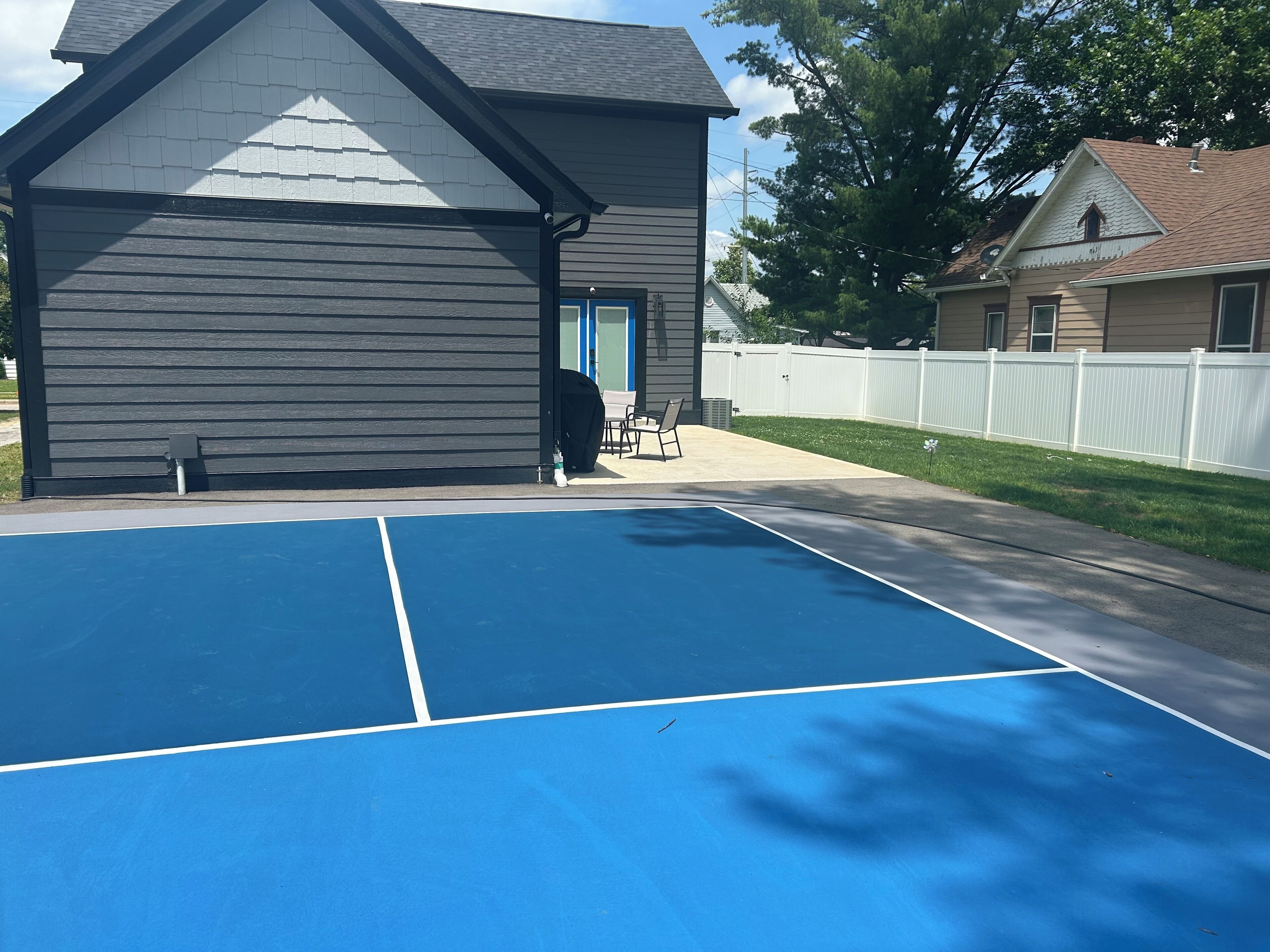 A residential area with a blue tennis court, a house with a dark exterior, and a white fence.