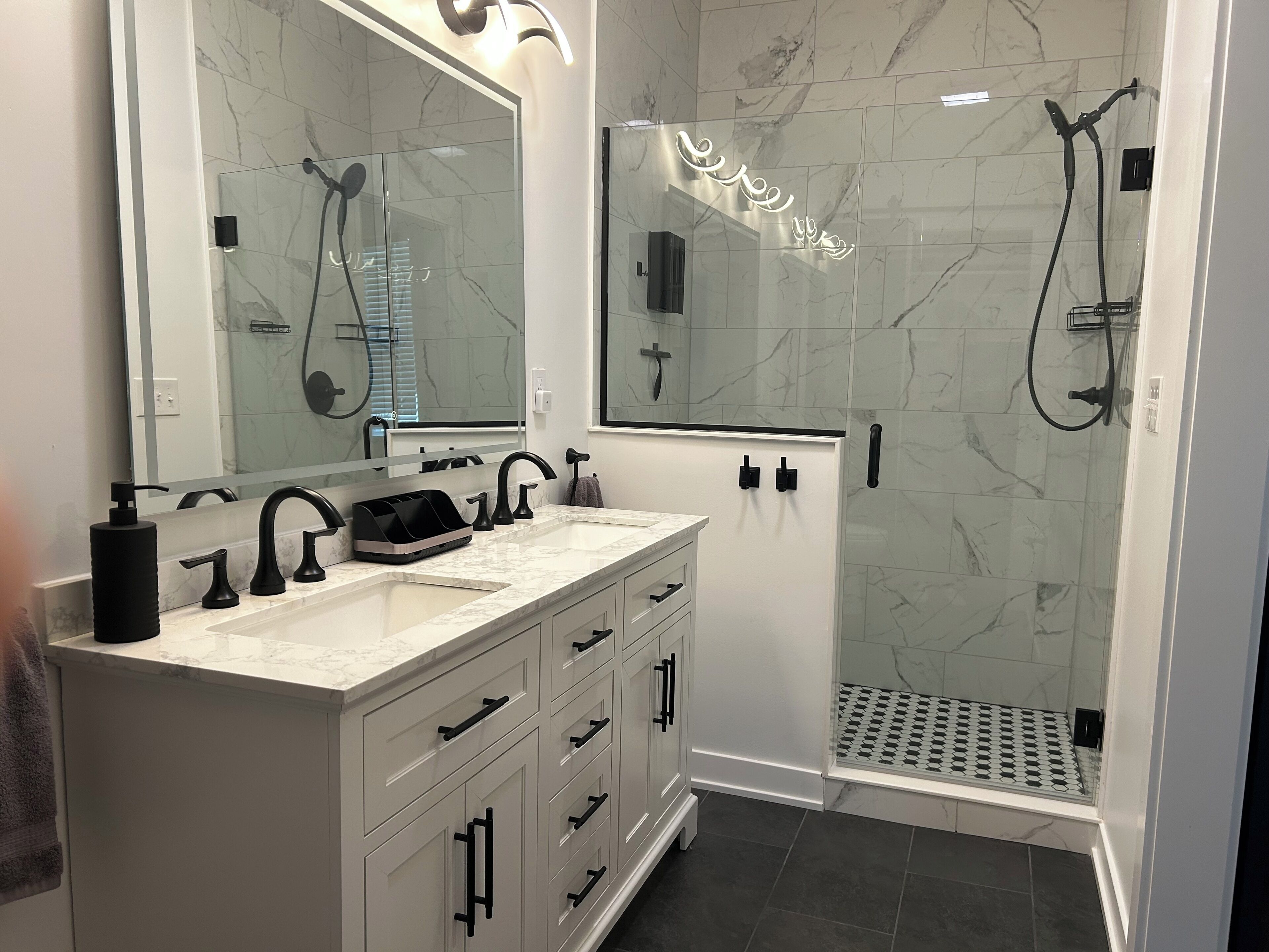 A modern bathroom with a double sink vanity, a large mirror, and a walk-in shower with a glass door.