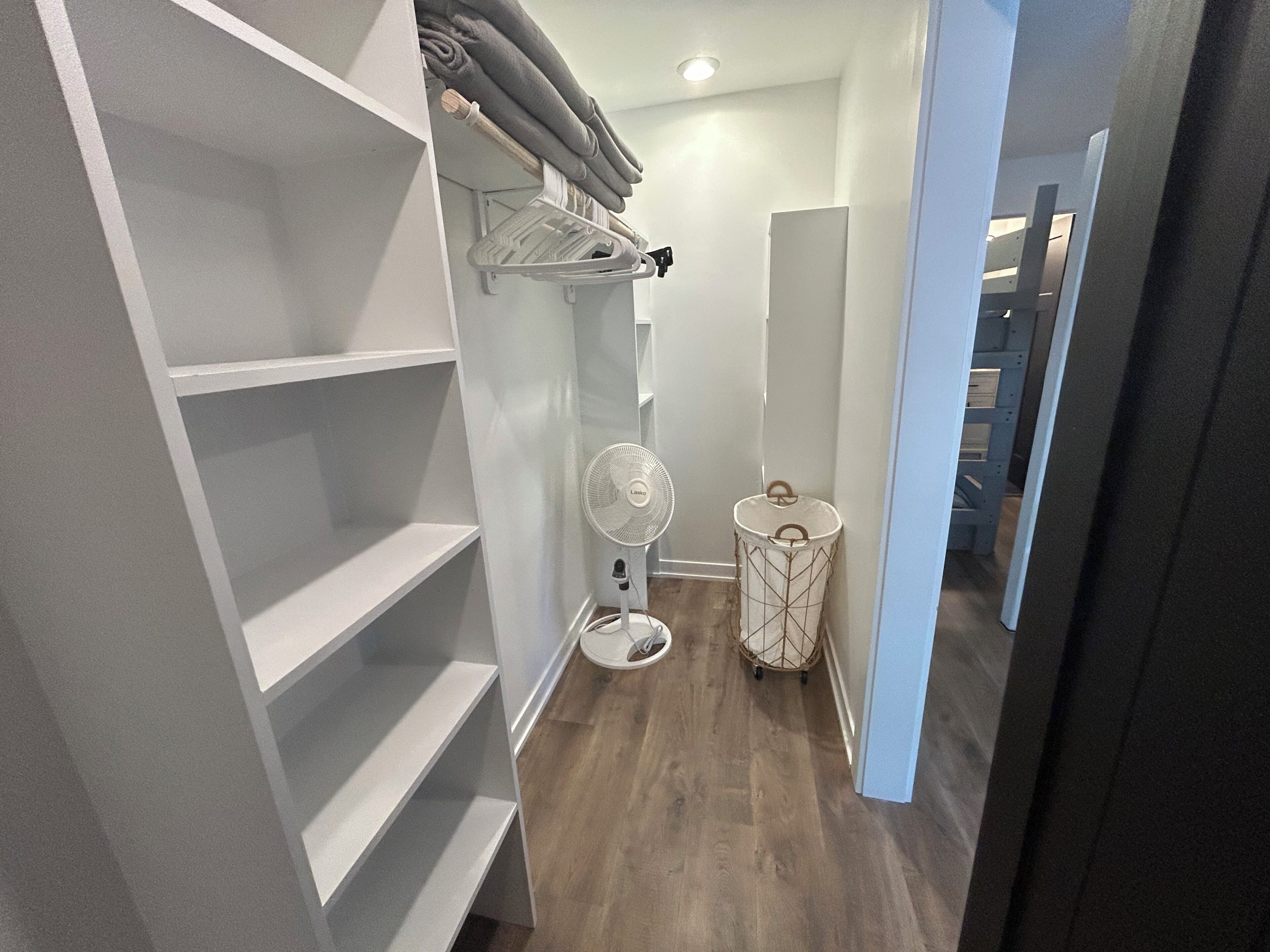 A narrow hallway with a white closet on the left, a white trash bin, and a small fan on the right.