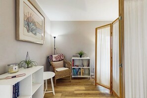 A cozy living room with a wicker chair, a small white table, a bookshelf, and a framed artwork on the wall. - 3BR Waterview - Deck - Washer Dryer (Des Moines)