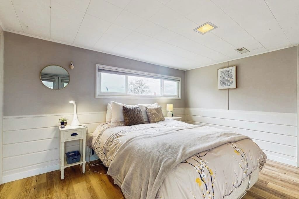 Une chambre à coucher comprenant un lit, des tables de chevet, une fenêtre, un miroir et un tableau accroché au mur.
