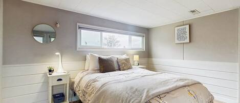 Une chambre à coucher comprenant un lit, des tables de chevet, une fenêtre, un miroir et un tableau accroché au mur.