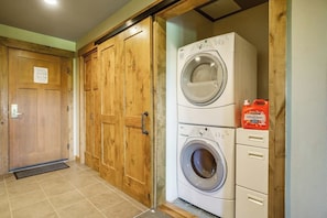 A laundry room with a front-loading washer and dryer, wooden doors, and a tiled floor. - Elegant 2BR Golf Course View Suncadia Resort Dog (Cle Elum)