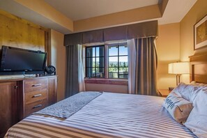 A hotel room with a bed, a television, a window with curtains, and a view of the outdoors. - Elegant 2BR Golf Course View Suncadia Resort Dog (Cle Elum)