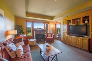 Una sala de estar con sofá, sillón, mesa de centro, chimenea, televisor y armarios de madera.