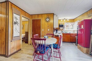 Eine kompakte Küche mit Holzvertäfelung, einem Esstisch mit Stühlen, einem Kühlschrank und einer Mikrowelle.