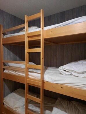 A bunk bed with a wooden ladder, white bedding, and a wooden wall.