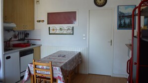 Een kleine keuken met een eettafel, een klok en een deur met een raam.