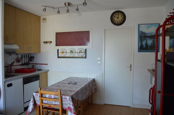 A compact kitchen with a dining table, a clock, and a door with a window.