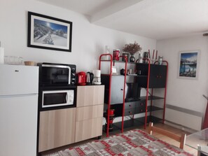 Una cocina compacta con microondas, cafetera y una tetera roja sobre la encimera.