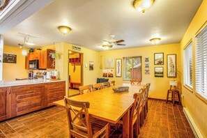 Een eetgedeelte met een houten tafel en stoelen, een keuken met houten kastjes, en een plafondventilator.