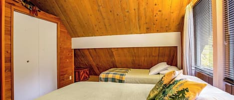 A bedroom with a sloped ceiling, a bed with a quilted mattress, two pillows, a bedside table, and a window with blinds.