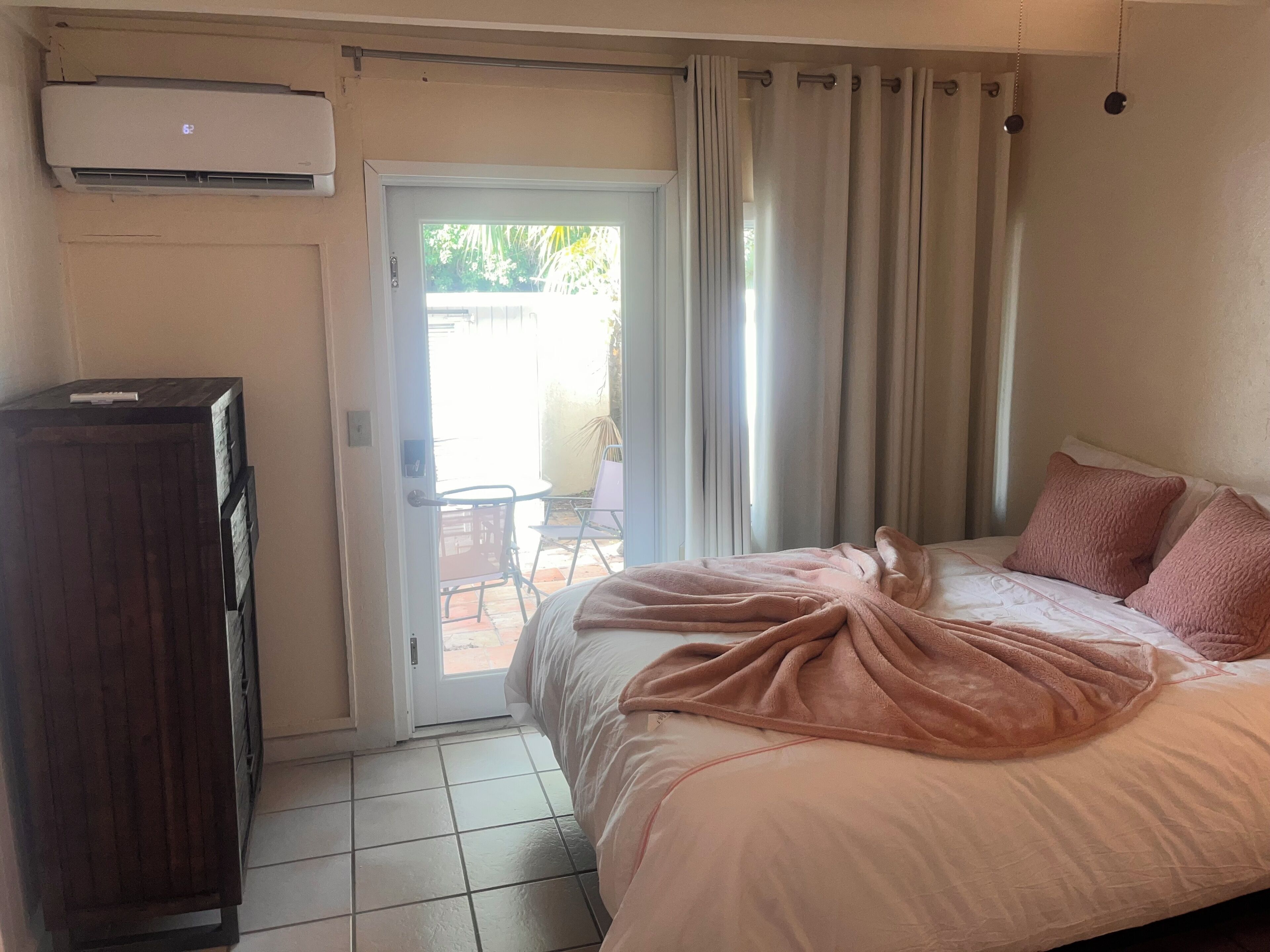 A bedroom with a bed, a wooden cabinet, a sliding glass door leading to a patio, and an air conditioning unit.